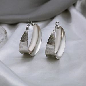 Minimalist silver brushed metal C-shape hoop earrings on elegant silk fabric background