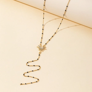 Detail shot of a golden Y-shaped long necklace with black beads and a sun pendant