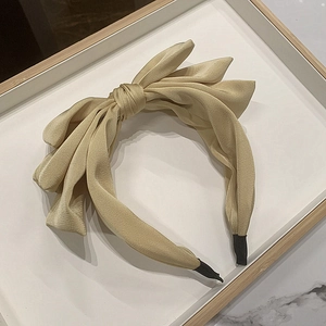 Detail view of cream fabric headband featuring a layered 3D bow on a white tray