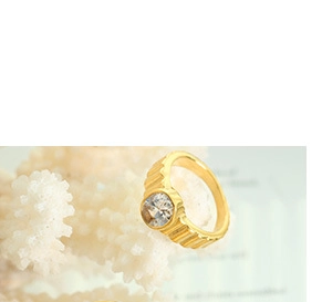 Détail d'une bague dorée côtelée avec pierre ronde claire sur fond de corail blanc