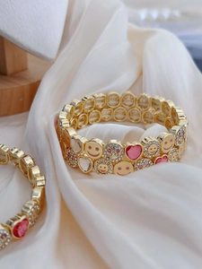Detail of gold-tone flower and smile face bracelet on elegant white silk fabric