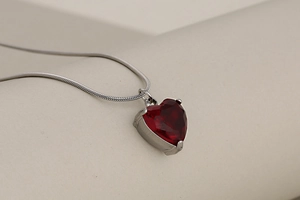 Detail of red heart crystal pendant with silver snake chain on a minimalist display