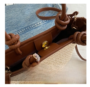 Detailed close-up of the metal magnetic buckle and brown leather trim on straw tote bag