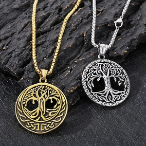 Close-up of gold and silver Tree of Life pendants with box chains on a dark stone surface