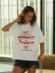 T-shirt bianca oversize con stampa rossa Travel Addict in un ambiente moderno