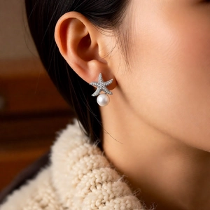 Close-up of star pearl earrings with zircon inlay worn by a model in soft lighting
