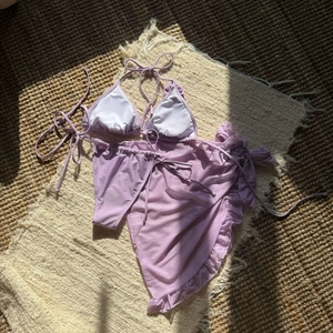 Close-up of light purple 3-piece bikini set with sheer mesh beach skirt and ruffle detail