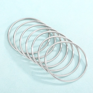 Set of seven minimalist polished silver stainless steel bangles on a blue textured surface