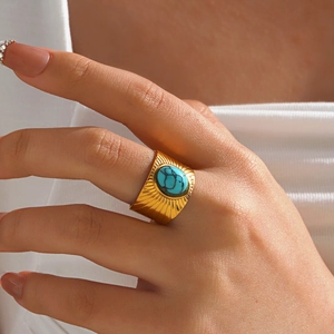 Golden wide band ring with sunburst engraving and oval turquoise stone on model's hand