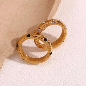 Detail von 18K vergoldeten Ringen mit weißen und grünen Zirkonia auf feuchtem Stein