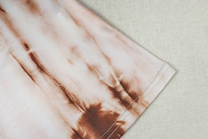 Detail view of double-stitched hem and brown tie-dye texture on soft knit fabric