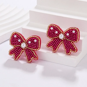 Detailed shot of handmade fuchsia and gold beaded bow earrings with white pearl accents