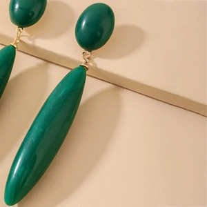Vintage emerald green teardrop dangle earrings with gold metal links on a beige surface