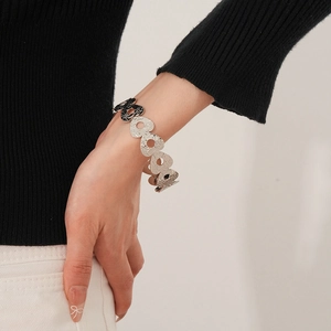 Detail showing hollowed-out heart patterns on silver metal bracelet worn by a model