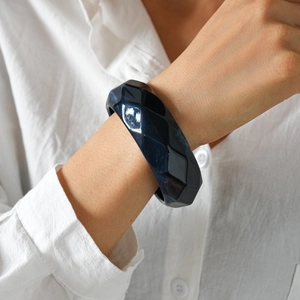 Detail eines dunkelblauen facettierten Acryl-Armreifs am Model mit weißem Leinenhemd