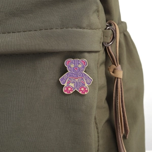 Close-up of purple cartoon bear enamel pin with colorful graffiti on a green fabric bag