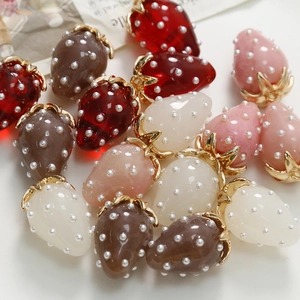 Red and pink resin strawberry pendants with pearls and golden leaves on white background
