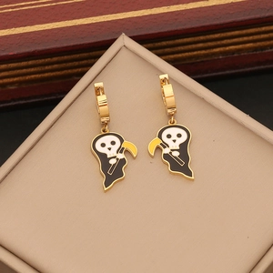 Close-up of golden reaper earrings with black and white enamel details on a beige pad