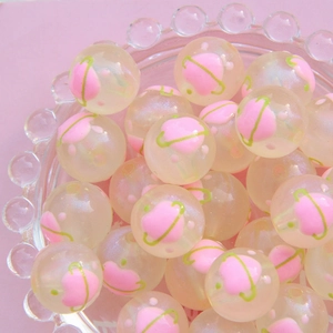 Détail de perles transparentes de 16mm avec cœurs roses et motifs verts dans un bol en verre