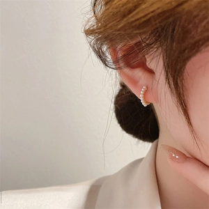 Close-up detail of small golden hoop earrings featuring delicate miniature white pearls