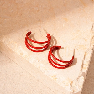 Detailed view of red triple-layered C-shaped hoop earrings on a textured stone surface