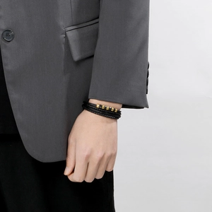 Men's multilayer braided leather bracelet with gold and black steel beads on a model's wrist
