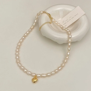 Detail of baroque pearl necklace with golden heart pendant on white ceramic tray