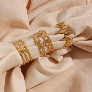 Close-up of three gold hollow stainless steel rings on premium beige silk fabric