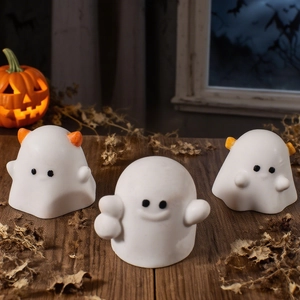 Three cute white Halloween ghost figurines with orange accents on dark wooden surface