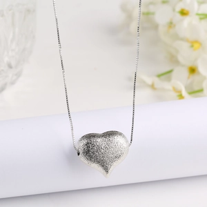 Macro detail of silver heart pendant with matte frosted finish on elegant box chain