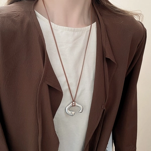 Detail of silver irregular C-shaped pendant necklace with dark brown leather cord on a model