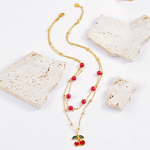 Double-layered gold necklace with vibrant red cherry pendant and decorative beads