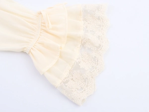 Detail of bell sleeves with lace embroidery and ruffled cuffs on a cream dress