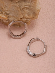 Vue macro de boucles d'oreilles créoles torsadées argent sur fond rose texturé