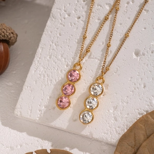 Minimalist gold Y-shaped necklace with pink and white zircon stones on stone background