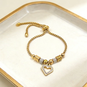 Adjustable gold heart charm bracelet with sparkling zircons on a white ceramic tray