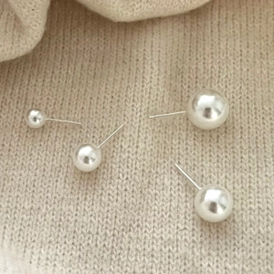 Macro detail of four sizes of ivory white pearl earrings on beige knit fabric background