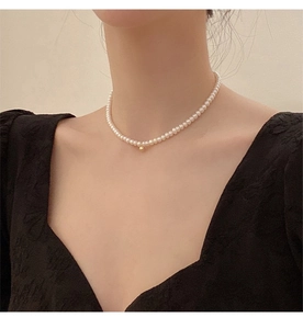 Close-up of elegant white pearl choker necklace with a gold ball pendant on a model