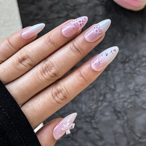 Détails d'ongles en amande dégradé rose avec nœuds 3D et décorations en perles