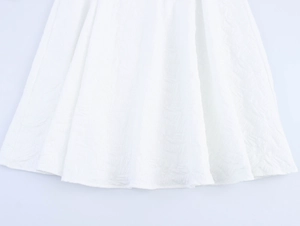 Detail of white dress hem featuring embossed jacquard texture and premium fabric drape