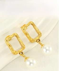 Close-up of golden square hollow earrings with white pearls on a textured background