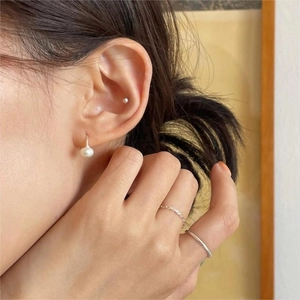 Close-up of minimalist freshwater pearl earrings and silver rings on model