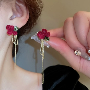 Dettaglio orecchini a fiore floccato rosso con nappe dorate indossati dalla modella