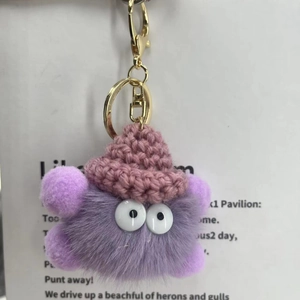 Detail of a purple fluffy monster keychain with pink knit hat and golden clasp hardware