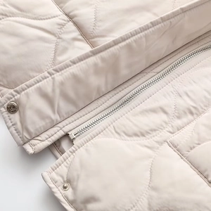 Detail of cream quilted jacket featuring metal zipper and wavy stitching pattern