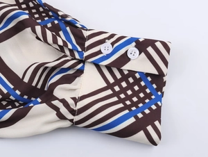 Close-up of dual white resin buttons on plaid chiffon shirt cuff with geometric pattern