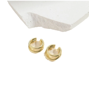 Minimalist double-layer gold ear cuffs in polished metal finish on white stone surface