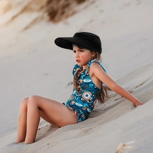 Side view of a little girl wearing a black wide brim sun visor hat on a sunny beach