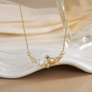 Detailed shot of a gold bird pendant with white pearl on a ceramic tray