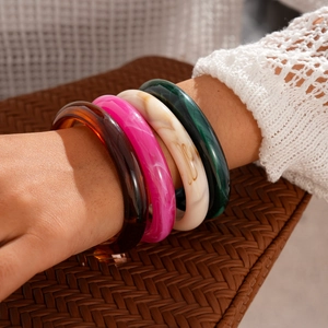 Gros plan de bracelets en acrylique empilés aux tons marbre et ambre sur le poignet